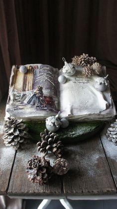 an open book on top of a wooden table with pine cones and snowflakes