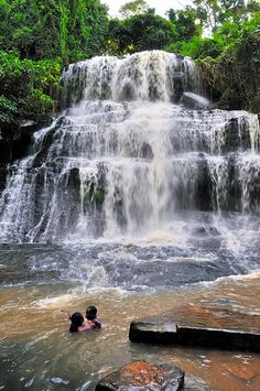 two people swimming in the water near a waterfall