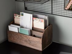 a wooden desk with two metal wire baskets on the wall above it and an open file box containing files