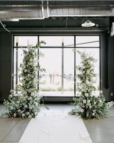 an indoor ceremony with white flowers and greenery on the floor, in front of large windows