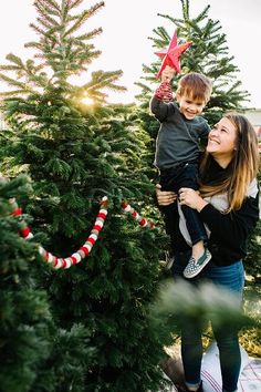 a woman holding a young boy in her arms while standing next to a christmas tree