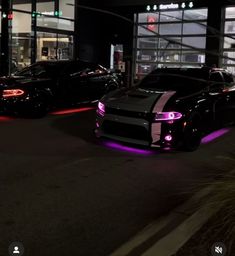 two cars parked in front of a building at night with neon lights on the windows