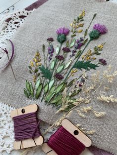 two wooden pins with flowers on them sitting next to some thread and twine spools