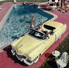 an old yellow car parked next to a swimming pool with people in the back seat