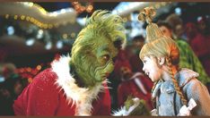 two children dressed as grinen and the grine is talking to each other in front of christmas lights