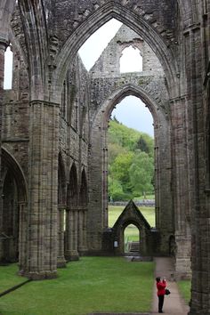 a person standing in the middle of an old building with stone arches and green grass