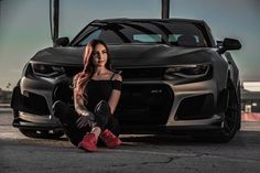 a woman sitting on the ground next to a car