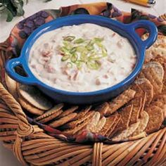 a bowl of dip and crackers on a wicker platter with other snacks