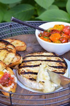 grilled sandwiches with tomatoes, cheese and bread on a round metal tray next to a bowl of salad