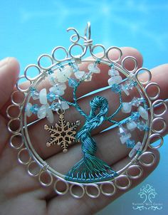 a hand holding a wire wrapped brooch with snowflake and crystal beads on it