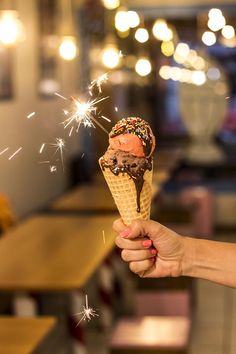 a person holding an ice cream cone with chocolate and sprinkles in it