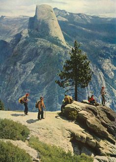 three people standing on top of a mountain with trees and mountains in the back ground