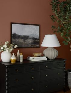 a black dresser topped with vases and flowers next to a painting on the wall