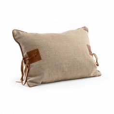 a beige pillow with leather straps on the front and back, sitting on a white surface