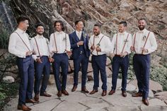 a group of men standing next to each other in front of a stone wall wearing ties