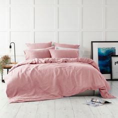 a bed with pink sheets and pillows in a white room next to a potted plant