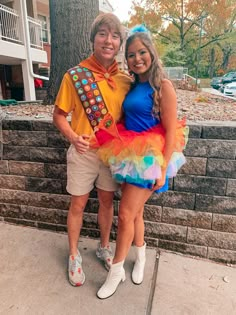 a man and woman dressed in costumes standing next to each other on the sidewalk near a tree