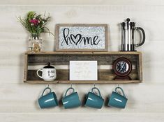 a shelf with coffee cups and mugs on it, next to a sign that says home