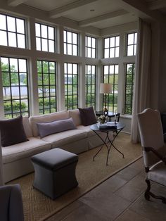 a living room filled with lots of windows next to a couch and chair in front of a table