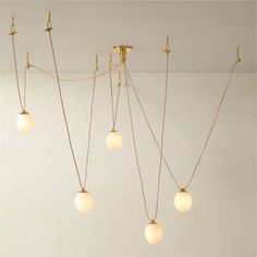 A push-and-pull between hard and soft, architectural and feminine, the striking Augustine chandelier designed by goop hangs like jewelry from the ceiling. Inspired by bespoke designer lighting installations, the multi-pendant chandelier features delicate oval-shaped milk glass globes suspended by a rose gold cloth cord. The cord drapes gracefully from hook to hook, creating an unfussy composition with polished unlacquered brass elements that will develop the patina of a vintage find. CB2 exclusi Mid Century Modern Chandelier Dining, Cb2 Chandelier, Cb2 Lighting, Cb2 Decor, Funky Chandelier, Mcm Office, Modern Chandeliers For Living Room, Modern Chandelier Dining, Swag Chandelier