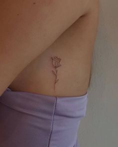 a small rose tattoo on the back of a woman's left side ribcage