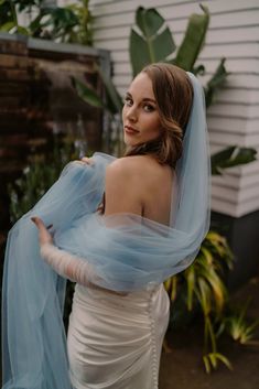 a woman in a wedding dress with a blue veil on her head and shoulders, looking off to the side