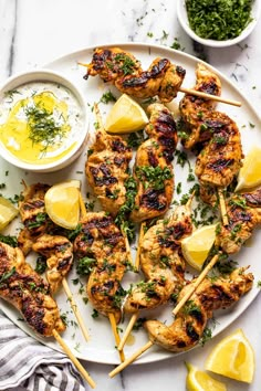 grilled chicken skewers with lemons and parsley on a white plate