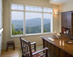 a desk and chair in front of a large window with mountains out the back ground