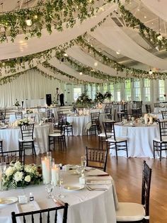 an indoor wedding reception with white linens and greenery hanging from the ceiling over tables