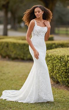 a woman in a white wedding dress standing on the grass with her hair blowing in the wind