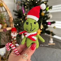 a crocheted grin face doll holding a candy cane in front of a christmas tree