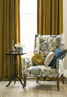 a chair and table in front of a window with yellow drapes on the windowsill