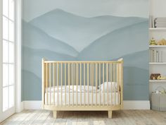 a baby's crib in front of a wall with mountains painted on it