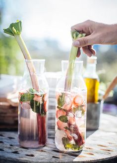 two vases filled with water and strawberries on top of a wooden table next to bottles