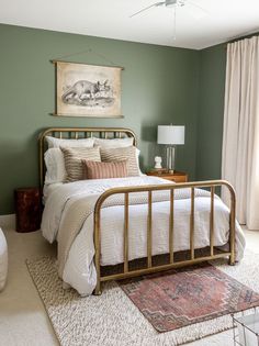 a bedroom with green walls and white bedding, rugs on the floor and a painting above the bed