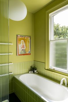 a bathroom with green tiles and a white bathtub in front of a painting on the wall