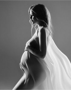 a pregnant woman in a white dress poses for a black and white photo with her hands on her hips