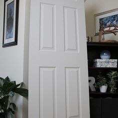 an open white door in a room with potted plants and pictures on the wall