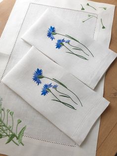 three embroidered napkins with blue flowers on them