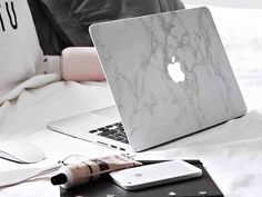 an apple laptop sitting on top of a bed next to a white pillow and other items