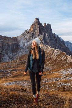 a woman standing on top of a grass covered field next to a tall mountain range