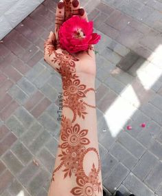 a woman's hand with henna on it holding a flower in the air