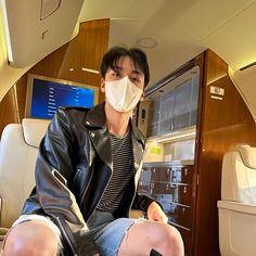 a man sitting on an airplane seat wearing a face mask and knee high leather boots