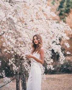 a woman standing in front of a tree with white flowers