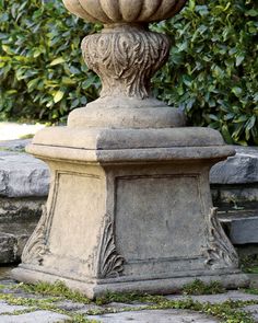 a large stone vase sitting on top of a cement pillar in front of some bushes