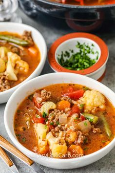 two bowls filled with soup and vegetables next to some chopsticks on the side