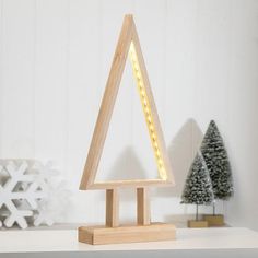 a small wooden christmas tree on a white shelf with snowflakes in the background