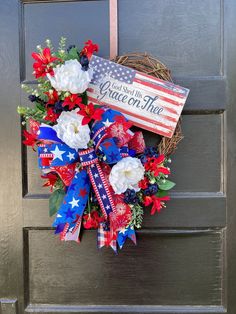 a patriotic wreath with flowers and an american flag ribbon hanging on the front door for memorial day