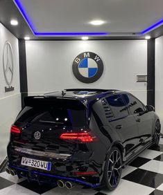 a black car is parked in front of a bmw logo on the wall and checkered floor