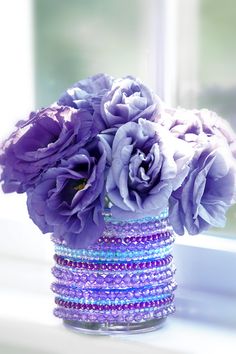 purple flowers are in a glass vase on a window sill with beaded bracelets